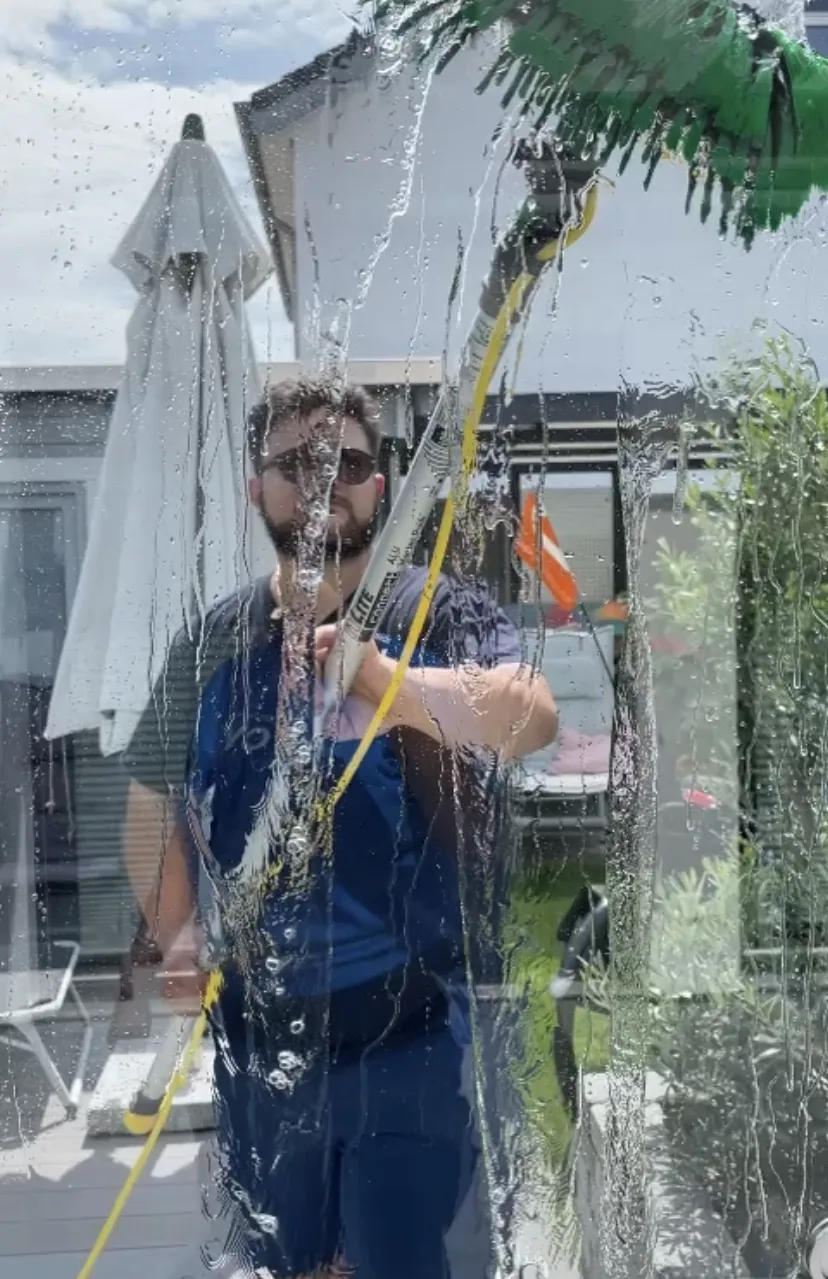 Gebäudereiniger mit Abzieher und Schlauch hinter einer nassen Glasscheibe