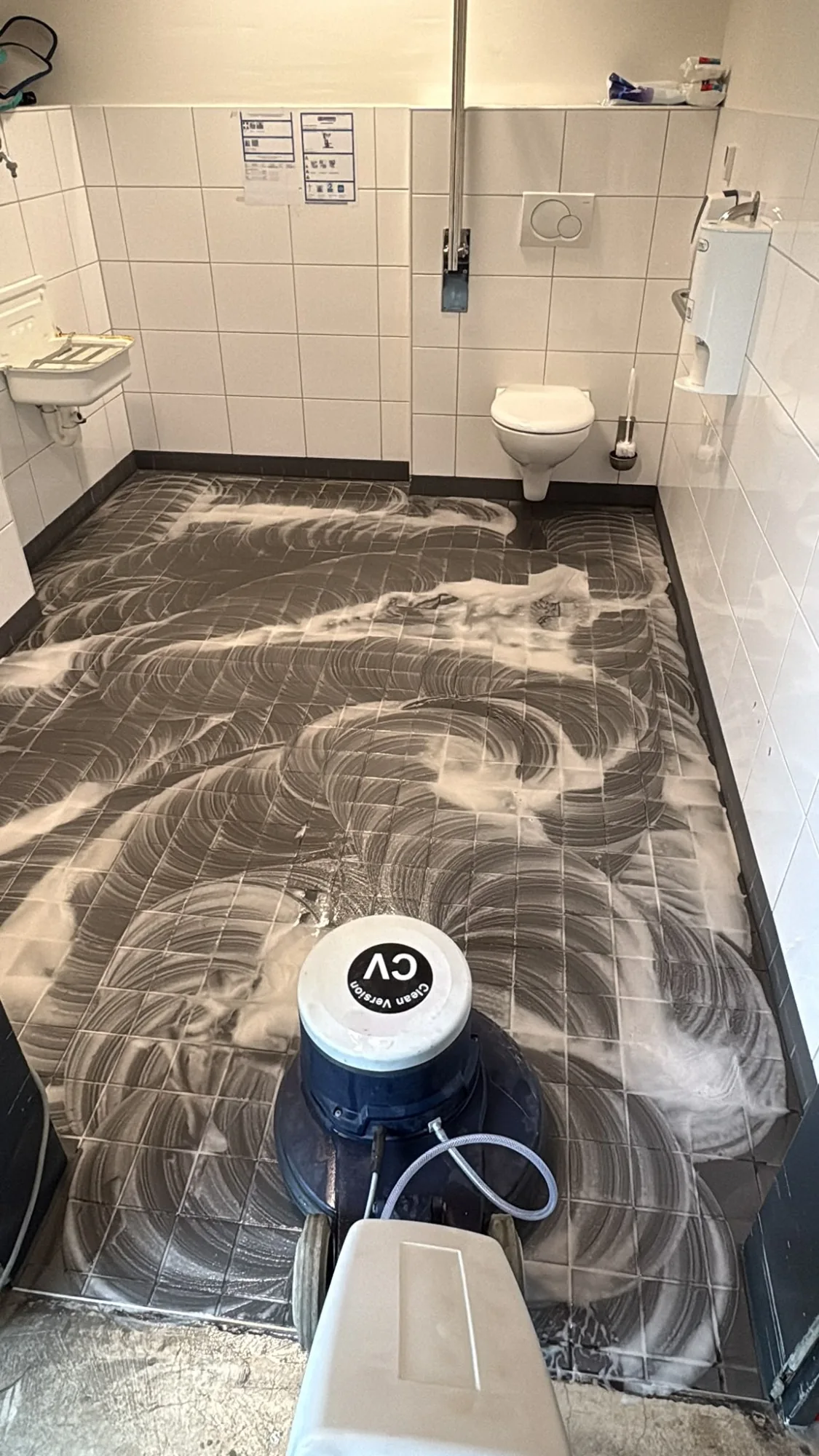 Grundreinigung eines gefliesten Sanitärraums, Schaum auf dem Boden und eine Reinigungsmaschine